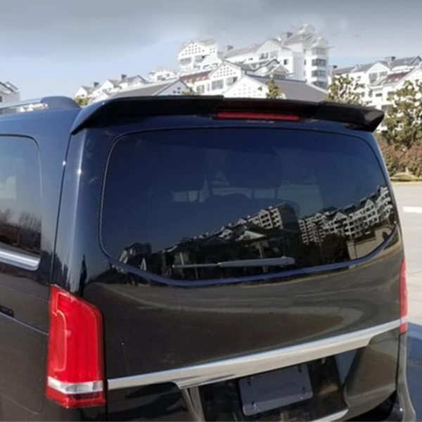 A black vehicle with tinted windows is parked, reflecting nearby white buildings with sloped roofs. The scene is set in a sunny, open outdoor area.