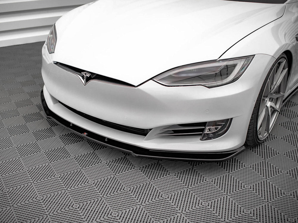 A white car with sleek headlights and a prominent front bumper rests on a textured, geometric-patterned floor in a clean, modern space.