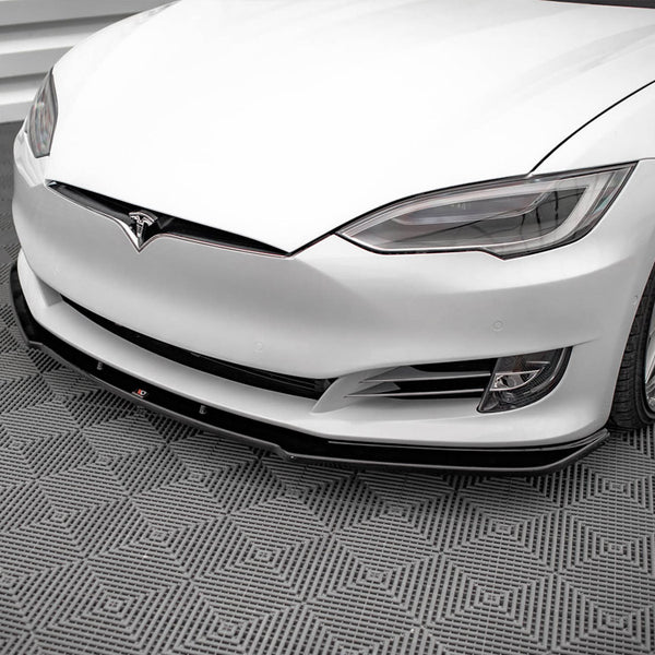 A white car with sleek headlights and a prominent front bumper rests on a textured, geometric-patterned floor in a clean, modern space.