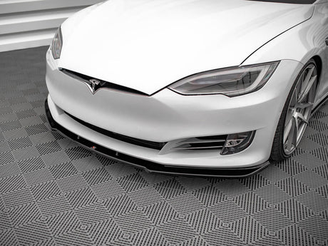 A white car with sleek headlights and a prominent front bumper rests on a textured, geometric-patterned floor in a clean, modern space.