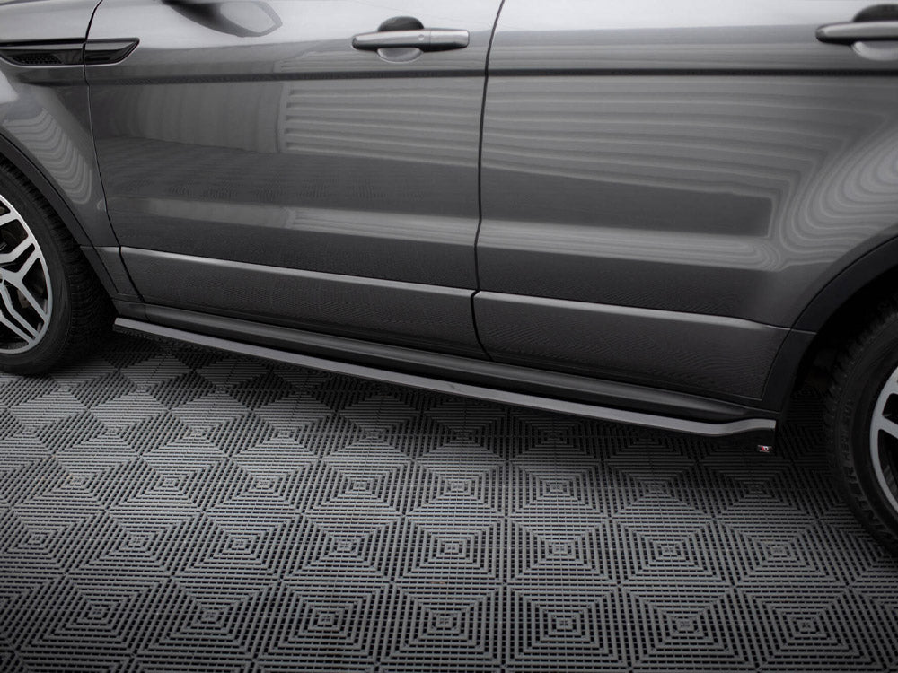 A gray car viewed from the side is parked on a textured, geometric-patterned surface in a well-lit indoor setting.