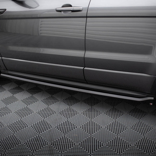 A gray car viewed from the side is parked on a textured, geometric-patterned surface in a well-lit indoor setting.