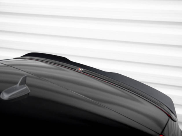 A glossy black car roof features a small antenna fin. The car is parked in front of a white, horizontally-lined wall, and a faint reflective logo is visible on the roof.