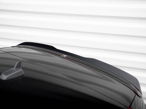 A glossy black car roof features a small antenna fin. The car is parked in front of a white, horizontally-lined wall, and a faint reflective logo is visible on the roof.