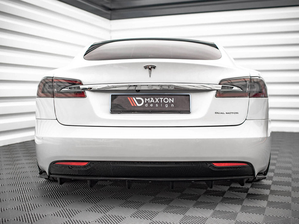 A white Tesla car is parked indoors on a textured floor, with "DUAL MOTOR" on the right and a "MAXTON design" plate in the center.