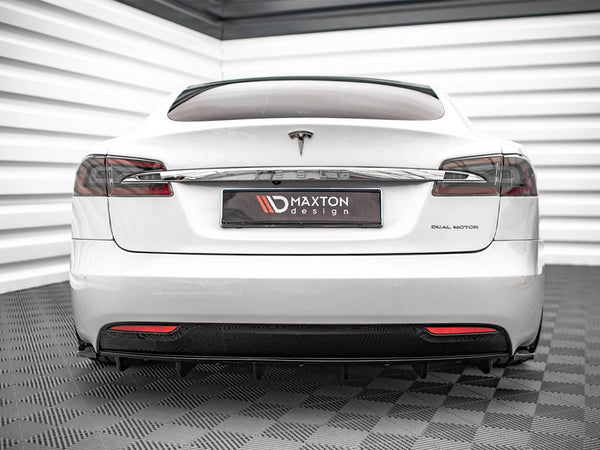 A white Tesla car is parked indoors on a textured floor, with "DUAL MOTOR" on the right and a "MAXTON design" plate in the center.