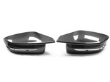 Two carbon fiber side mirror covers rest on a white surface. They feature a sleek, aerodynamic design with glossy finish and subtle contours, positioned symmetrically.