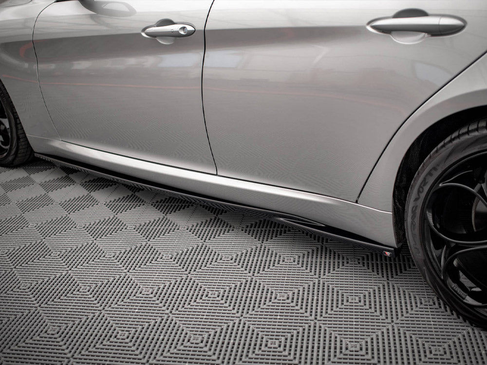 A silver car with black wheels is parked on a patterned, interlocking gray floor. The side profile emphasizes its sleek design and closed doors, with no text visible.