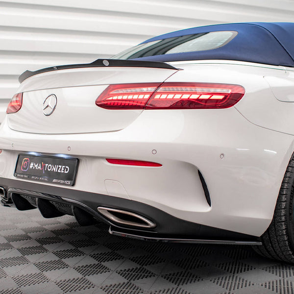 Car with white body and blue convertible top parked indoors; rear lights illuminated. The license plate reads "#MAXTONIZED" with logos for Mercedes-Benz and AMG. Ribbed white walls surround the vehicle.