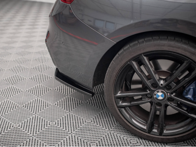 The image shows the rear wheel and bumper of a gray BMW car, parked on a patterned floor in an indoor space.