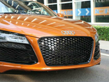 Orange sports car parked on a street, featuring a distinctive honeycomb grille and prominent Audi emblem. Background includes windows and a hedge, with Chinese text on visible signs.
