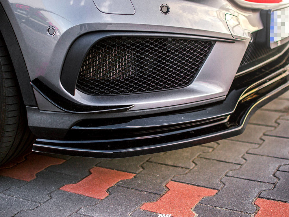 A grey car's front bumper with a black splitter and mesh grille is parked on a red and gray tiled surface.