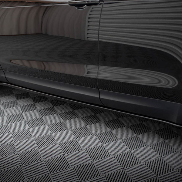 A black car rests on a geometric-patterned floor, reflecting striped wall patterns across its shiny side surface in an enclosed environment.