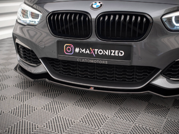 A grey car's front bumper with a prominent black grille displays a "#MAXTONIZED" plate above "CLAROMOTORS." The setting features a patterned grey floor and a modern, stylized background.