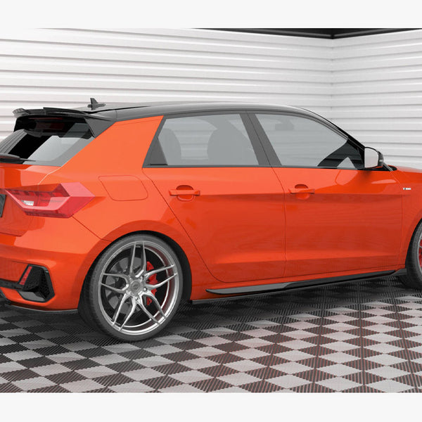 A bright orange hatchback car is parked on a checkered floor in a well-lit garage. The car features alloy wheels and a license plate reading "Maxton Design."