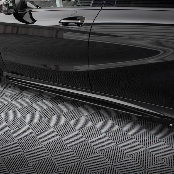 A sleek black car is parked on a geometric-patterned, gray floor. The car has tinted windows and black alloy wheels, reflecting a striped ceiling above.