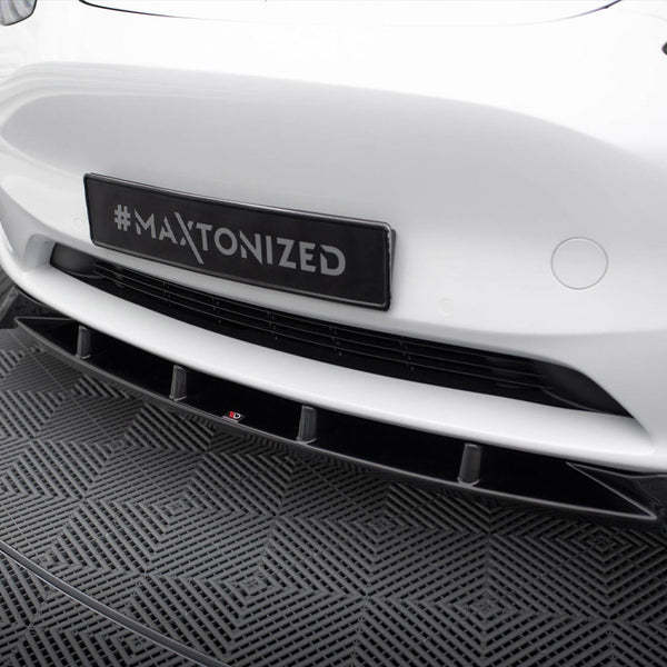A car's front bumper, displaying a hashtag "#MAXTONIZED" on a black license plate, is shown on a textured gray patterned floor in an indoor setting.