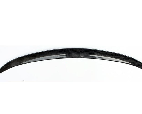 A curved carbon fiber spoiler rests against a plain white background, highlighting its glossy finish and aerodynamic design.