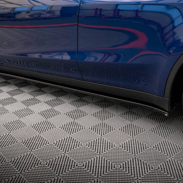 A blue car with sleek, reflective bodywork, parked on a textured geometric-patterned floor, shows partial view of a wheel and door on the right side.