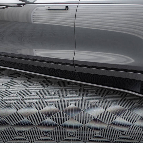 A shiny gray car door with sleek side mirror and wheel, parked on a geometric-patterned black and gray floor in a well-lit garage.