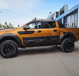 Orange pickup truck parked by a building, featuring rugged tires with "BFGoodrich All-Terrain T/A" text, against a clear sky backdrop. Notable black detailing adorns the vehicle's sides and wheel arches.