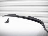 A sleek black car spoiler is mounted on a white vehicle roof, with a small shark-fin antenna nearby, set against a blurred horizontal striped background.