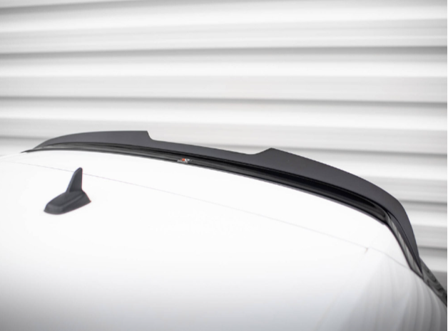 A sleek black car spoiler is mounted on a white vehicle roof, with a small shark-fin antenna nearby, set against a blurred horizontal striped background.