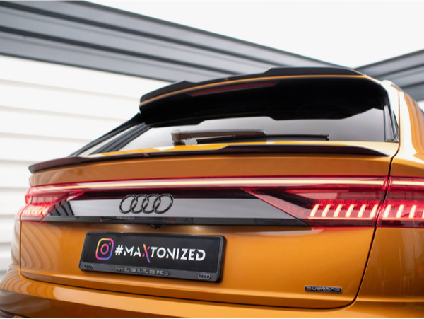 A gold Audi car shows its sleek rear, featuring illuminated taillights. It is parked outside a modern building. The license plate reads "@MAXTONIZED".