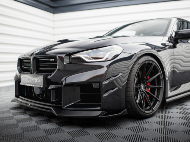 A sleek black sports car with a low front bumper and red-accented wheels is parked on a patterned floor against a backdrop of horizontal white and black lines.