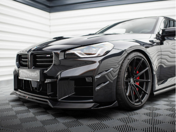A sleek black sports car with a low front bumper and red-accented wheels is parked on a patterned floor against a backdrop of horizontal white and black lines.