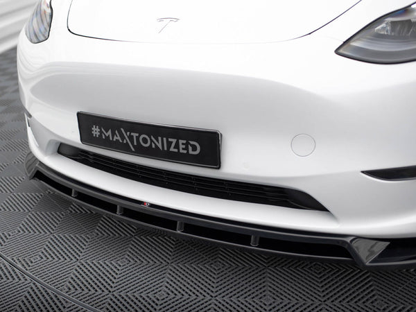 A car's front bumper with a "#Maxtonized" plate above a patterned floor, featuring sleek headlights and a prominent grille, set in a modern indoor space.