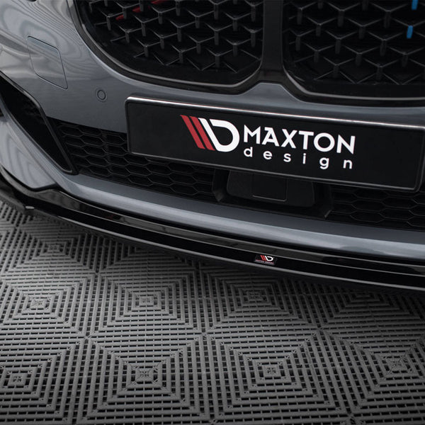 Car bumper features a "Maxton Design" logo, displayed on a patterned floor. The sleek, gray surface highlights an aesthetic grille, capturing a modern automotive design in a showroom setting.