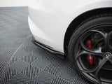 A white car's rear bumper is parked on a patterned grid floor. The black alloy wheel features red brake calipers labeled 