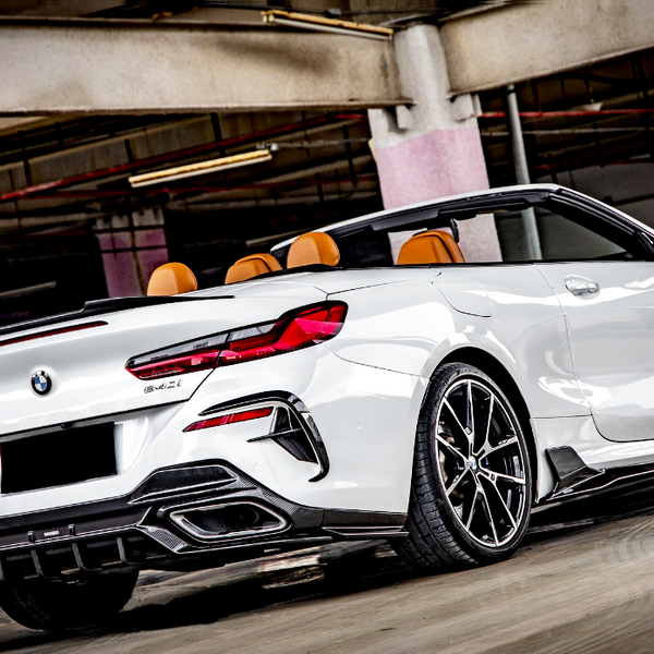 A white convertible sports car is parked in a dimly lit garage. The car features orange seats, intricate wheel designs, and visible branding on the rear, with a sleek, modern appearance.