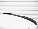 A black car roof spoiler is attached to a white car, set against a background of horizontal, white, metallic ridges.