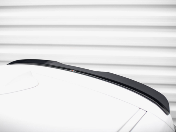A black car roof spoiler is attached to a white car, set against a background of horizontal, white, metallic ridges.