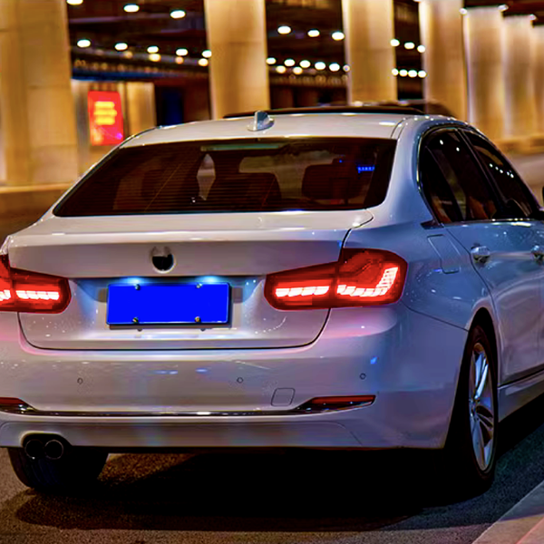 White car with illuminated taillights, parked in a well-lit tunnel, surrounded by other vehicles and glowing advertisements on nearby walls.