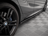 A black car tire is stationary next to a sleek vehicle body, reflecting a wavy pattern. The vehicle is parked on a textured, grid-like floor surface.