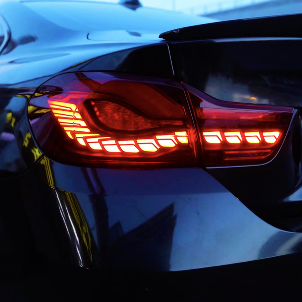 A car's taillight glows red in the evening light, with sleek body lines reflecting its urban surroundings. The context suggests an area with building reflections visible on the vehicle.