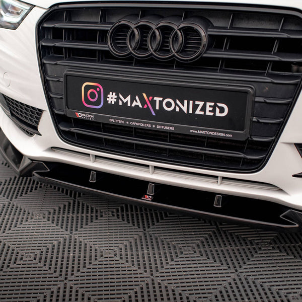 Car's front grille with Audi logo and license plate displaying text "#MAXTONIZED @MAXTONDESIGN.COM." It rests on a textured garage floor.
