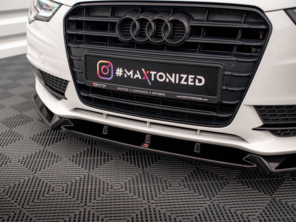 Car's front grille with Audi logo and license plate displaying text "#MAXTONIZED @MAXTONDESIGN.COM." It rests on a textured garage floor.