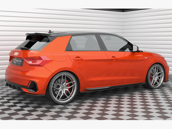 A bright orange hatchback car is parked on a checkered floor in a white-walled garage. It features silver alloy wheels and visible branding: "AUDI" and "Maxon Design".