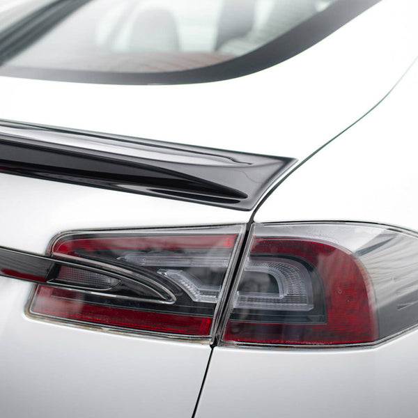 A white car with a sleek black spoiler is parked, highlighting its angular, modern taillight design. The context suggests a clean, bright environment.