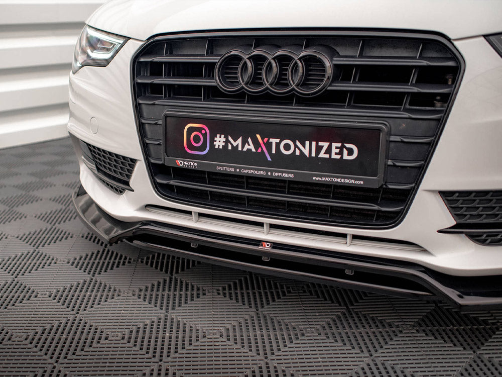 Car front bumper with Audi logo displays a license plate reading "#MAXTONIZED." The car is parked on a textured floor, surrounded by white paneling. Text: "SPLITTERS * CAPSPOILERS * DIFFUSERS * MAXTONDESIGN.COM."