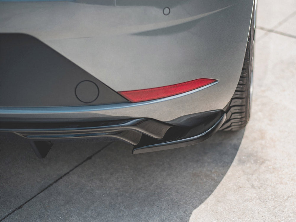 A car's rear bumper with a red reflector is parked on a sunlit, textured concrete surface, highlighting the curvature and tire tread.