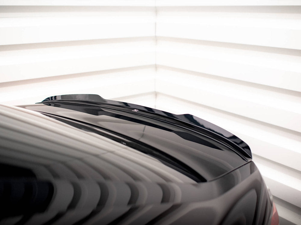 A sleek black car roof with a subtle spoiler is angled in a well-lit, white-striped room, casting dynamic reflections across its surface.