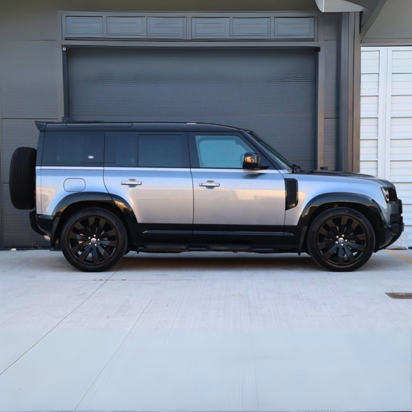 The vehicle, a silver SUV, is parked beside a large, closed industrial door. The setting is an urban area with smooth concrete ground and a modern building façade.