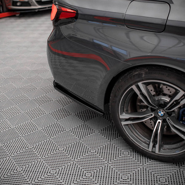 A dark gray car's rear wheel is stationary on a patterned garage floor, with a red vehicle lift partially visible in the background.