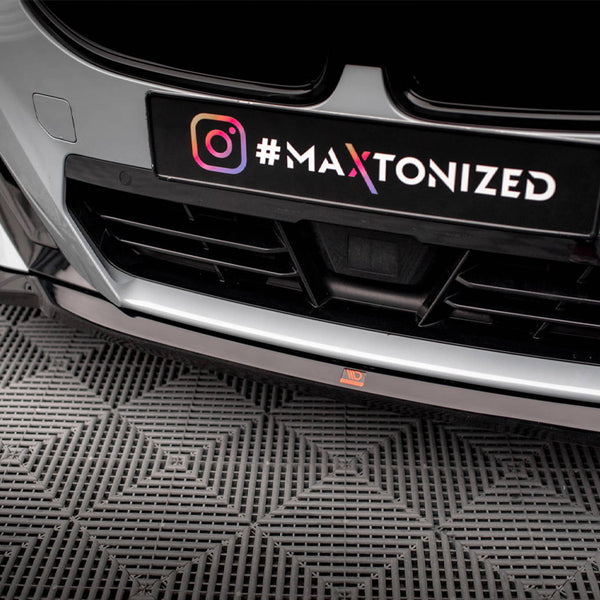 Car front bumper with a sleek design features a black license plate displaying an Instagram logo and the text "#MAXTONIZED." It is situated on a textured, patterned floor.