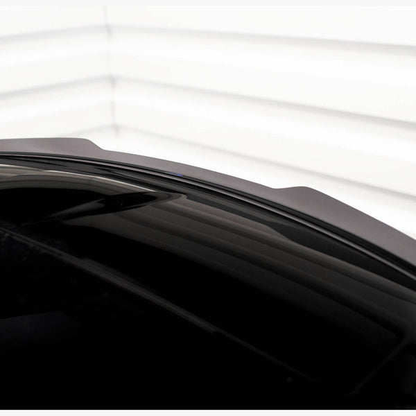 A sleek, shiny black car roof with a subtle aerodynamic spoiler is shown. The background consists of white horizontal paneling, creating a minimalistic and modern setting.